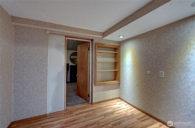 spare room featuring built in features, baseboards, and wood finished floors