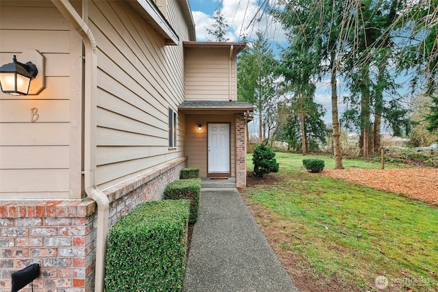 entrance to property with brick siding and a yard