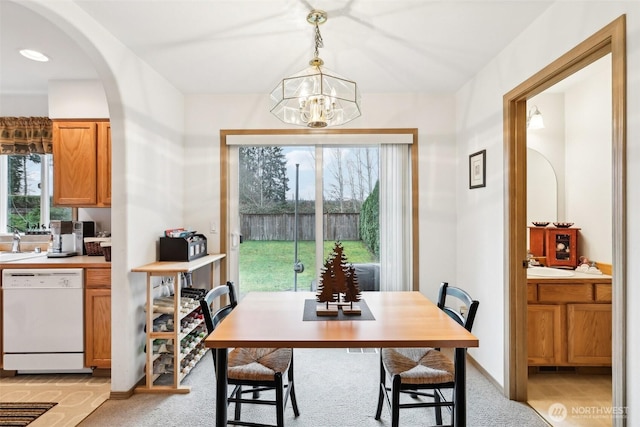 dining space with arched walkways, baseboards, light colored carpet, and an inviting chandelier