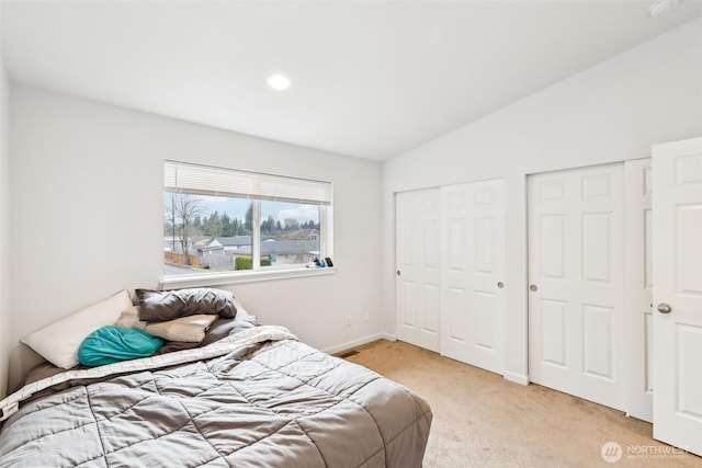 bedroom featuring vaulted ceiling, baseboards, light colored carpet, and multiple closets