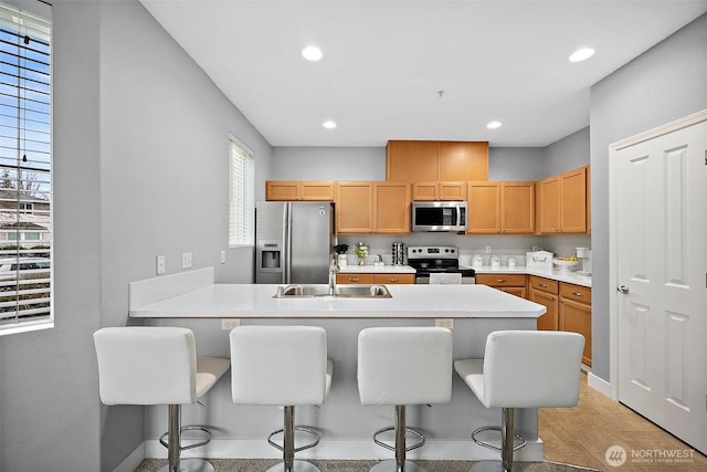 kitchen with a peninsula, a breakfast bar, a sink, light countertops, and appliances with stainless steel finishes