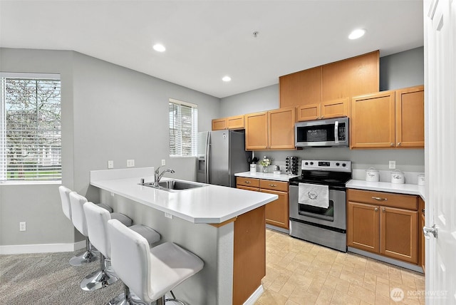 kitchen featuring a breakfast bar, light countertops, appliances with stainless steel finishes, a sink, and a peninsula