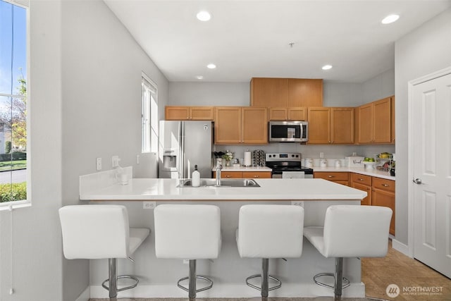 kitchen featuring stainless steel appliances, a sink, recessed lighting, a kitchen bar, and light countertops