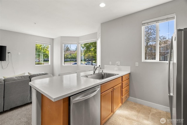 kitchen with stainless steel appliances, a sink, a healthy amount of sunlight, open floor plan, and baseboards