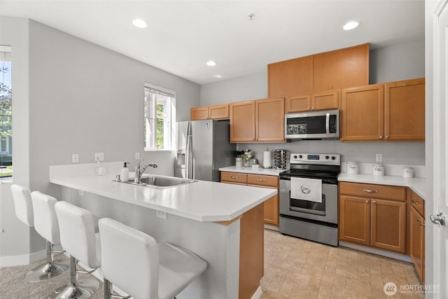 kitchen with a sink, a breakfast bar, light countertops, appliances with stainless steel finishes, and recessed lighting