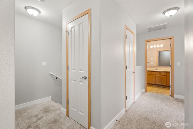 hall with visible vents, baseboards, light carpet, and a sink