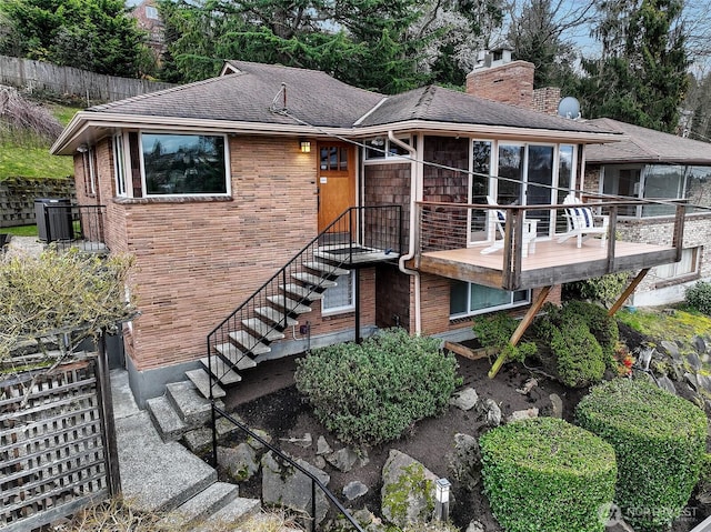 view of front of property featuring brick siding, a chimney, central air condition unit, a sunroom, and stairs