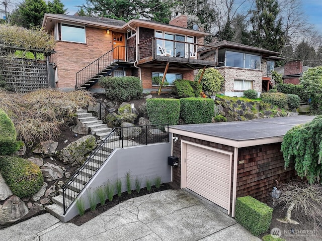 view of front of house with driveway, a garage, a chimney, stairway, and brick siding