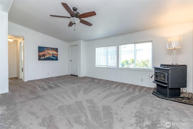 unfurnished living room featuring vaulted ceiling, carpet floors, ceiling fan, and a wood stove