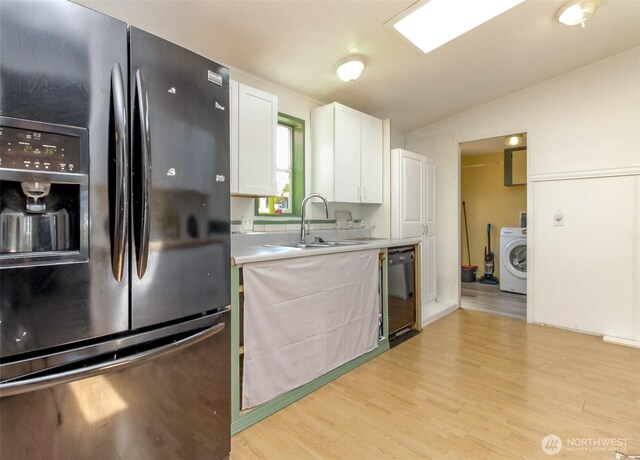 kitchen featuring light countertops, a sink, black appliances, washer / dryer, and white cabinetry