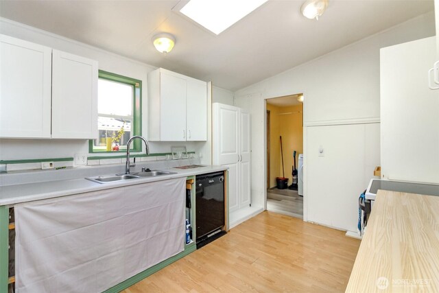kitchen featuring black dishwasher, white cabinets, a sink, and light countertops