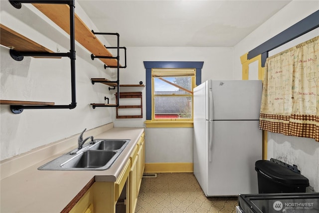 kitchen featuring baseboards, light floors, light countertops, freestanding refrigerator, and a sink