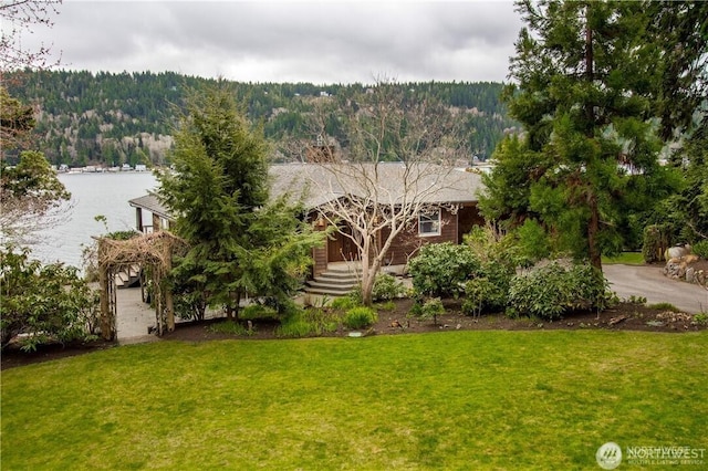 view of front of home with a front lawn, a water view, and a forest view