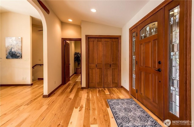 entryway with baseboards, arched walkways, lofted ceiling, light wood-style floors, and recessed lighting