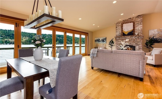 dining space with a large fireplace, light wood-style flooring, vaulted ceiling, and recessed lighting