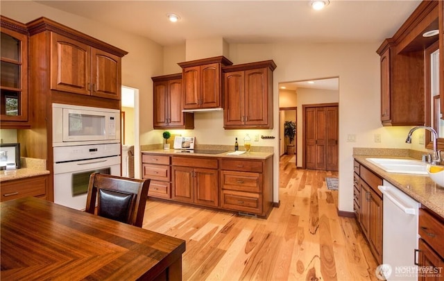 kitchen with light wood finished floors, white appliances, a sink, and glass insert cabinets