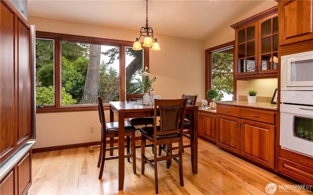 dining area with lofted ceiling, a notable chandelier, light wood-style flooring, and baseboards