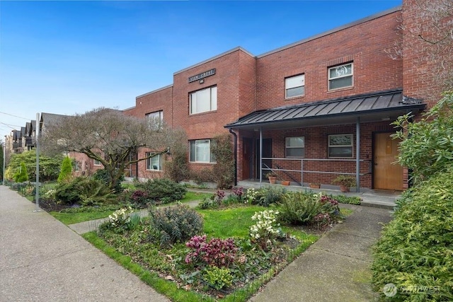 view of front of property featuring metal roof, brick siding, a standing seam roof, and a porch