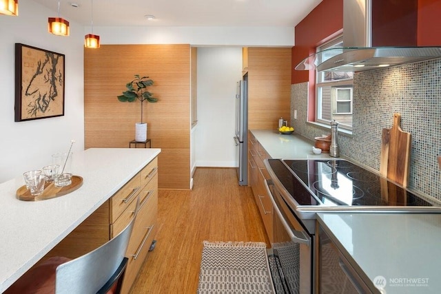 kitchen with pendant lighting, stainless steel appliances, backsplash, light wood-style flooring, and wall chimney exhaust hood