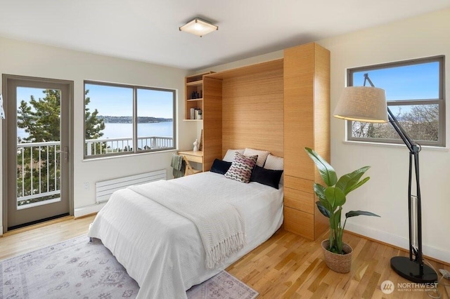 bedroom with access to exterior, light wood finished floors, a water view, radiator heating unit, and baseboards