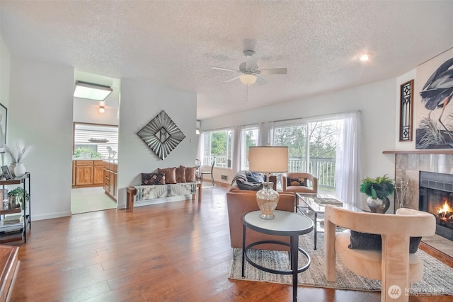 living area featuring wood-type flooring, a textured ceiling, ceiling fan, and a fireplace