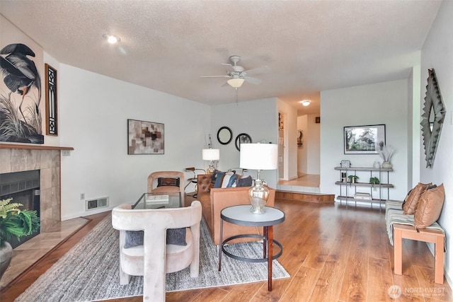 living room with wood finished floors, visible vents, a fireplace, ceiling fan, and a textured ceiling