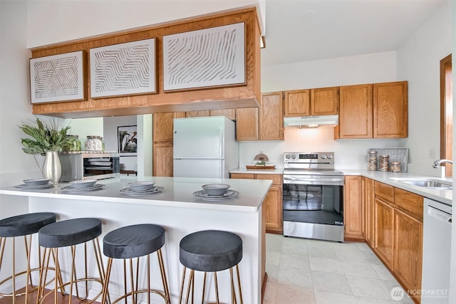 kitchen with a breakfast bar, a sink, under cabinet range hood, white appliances, and light countertops