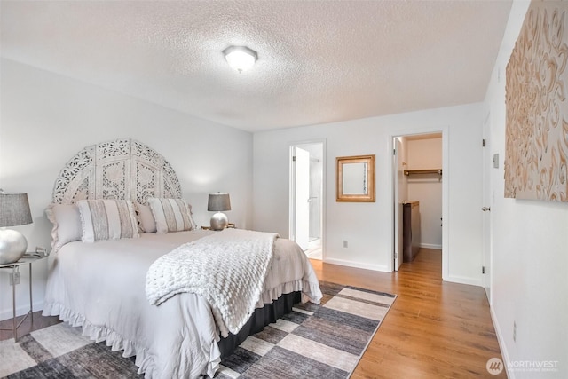 bedroom featuring a walk in closet, baseboards, a textured ceiling, and wood finished floors