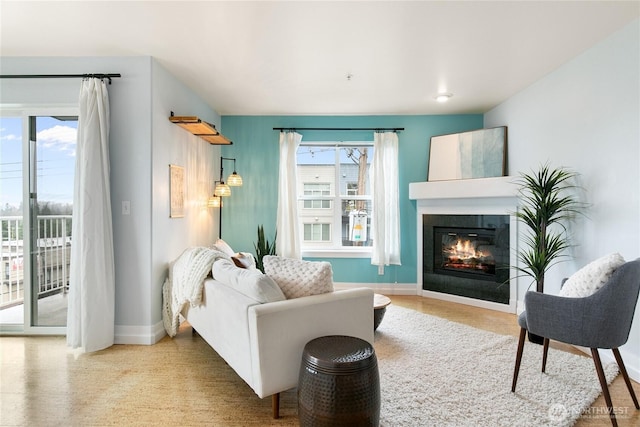 living area with a glass covered fireplace, baseboards, and a wealth of natural light