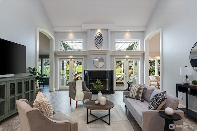 living area featuring arched walkways, a fireplace with flush hearth, wood finished floors, french doors, and high vaulted ceiling