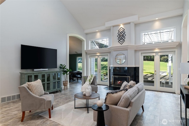 living area featuring high vaulted ceiling, visible vents, a glass covered fireplace, and french doors