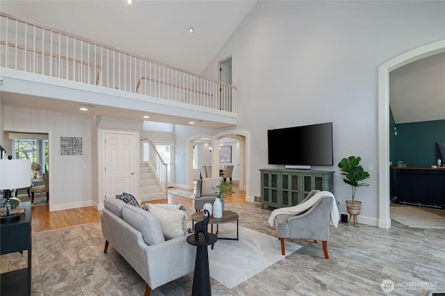 living room with arched walkways, high vaulted ceiling, stairway, and baseboards