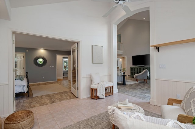 interior space with arched walkways, light tile patterned floors, a towering ceiling, a ceiling fan, and wainscoting