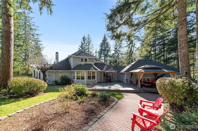 rear view of property with a deck, a yard, a chimney, and a gazebo