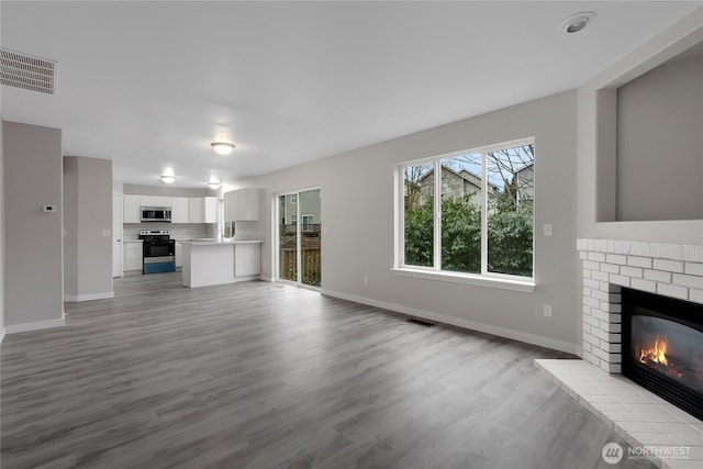 unfurnished living room with visible vents, a fireplace, baseboards, and wood finished floors