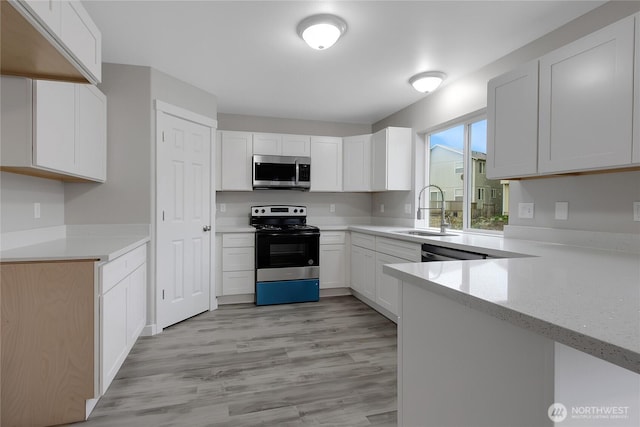 kitchen with appliances with stainless steel finishes, a sink, white cabinetry, and light wood-style floors