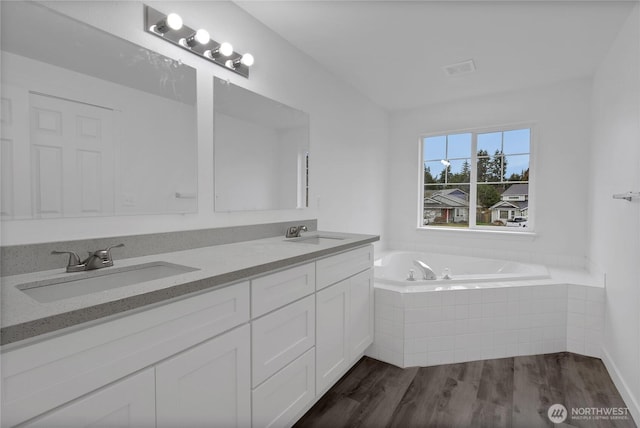 bathroom featuring a bath, double vanity, a sink, and wood finished floors