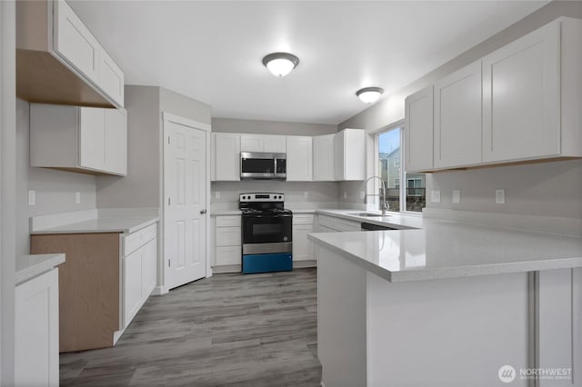 kitchen featuring range with electric cooktop, stainless steel microwave, a peninsula, light countertops, and a sink