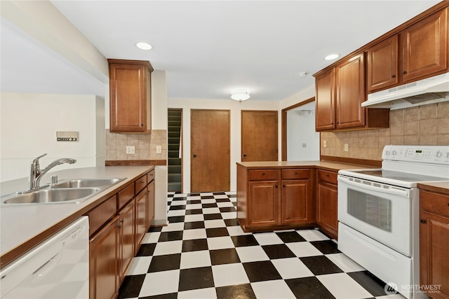 kitchen featuring white appliances, dark floors, a peninsula, under cabinet range hood, and a sink