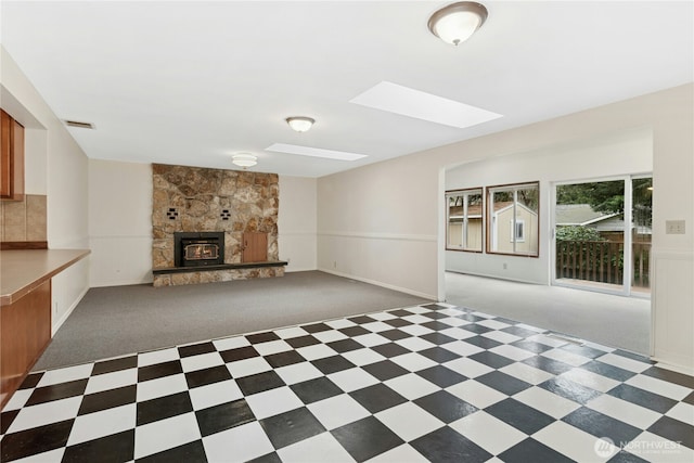 unfurnished living room featuring a skylight, visible vents, carpet flooring, and a wainscoted wall