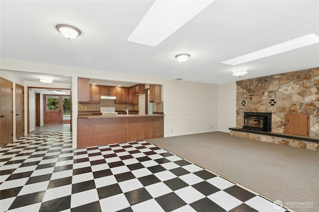 kitchen with a skylight, range, decorative backsplash, brown cabinets, and under cabinet range hood