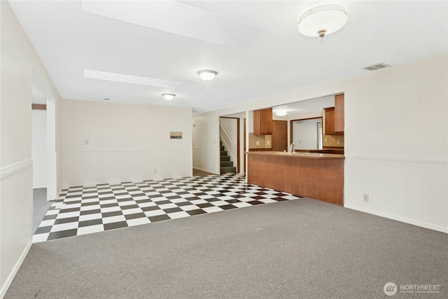 carpeted spare room featuring wainscoting, visible vents, and stairway