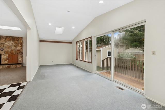 empty room with visible vents, lofted ceiling with skylight, carpet, a fireplace, and recessed lighting