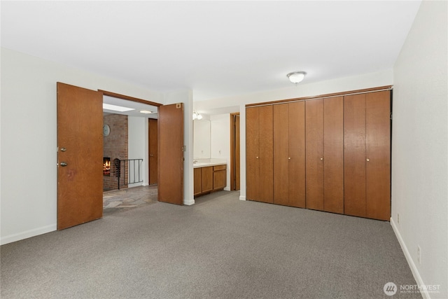 unfurnished bedroom featuring a fireplace, baseboards, a closet, and light colored carpet