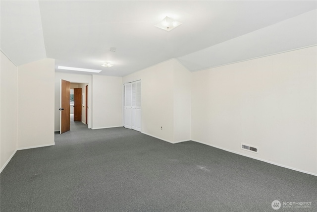 spare room featuring dark carpet, baseboards, visible vents, and vaulted ceiling