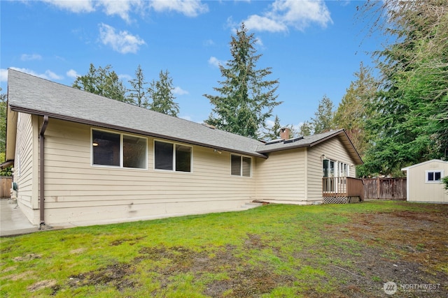 rear view of property featuring a deck, an outdoor structure, fence, a lawn, and a storage unit