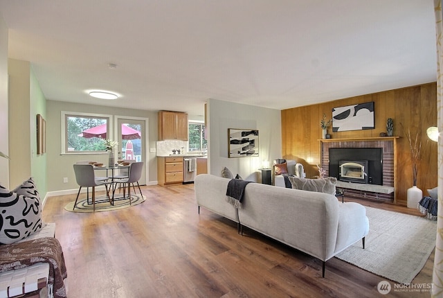 living room featuring a fireplace, light wood-style floors, wood walls, and a healthy amount of sunlight