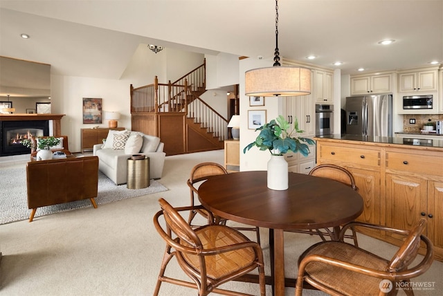 dining space with light carpet, recessed lighting, stairway, and a glass covered fireplace