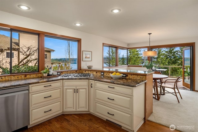 kitchen with a peninsula, cream cabinets, appliances with stainless steel finishes, and dark wood-type flooring