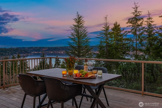 deck at dusk with a water view and outdoor dining space